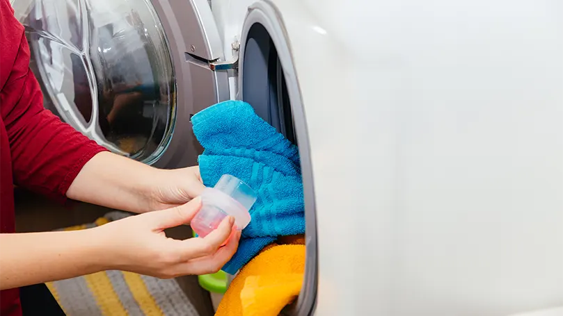 An image of a woman pouring a detergent in a washing machine.