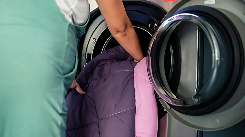An image of a woman putting a weighted blanket in washing machine.