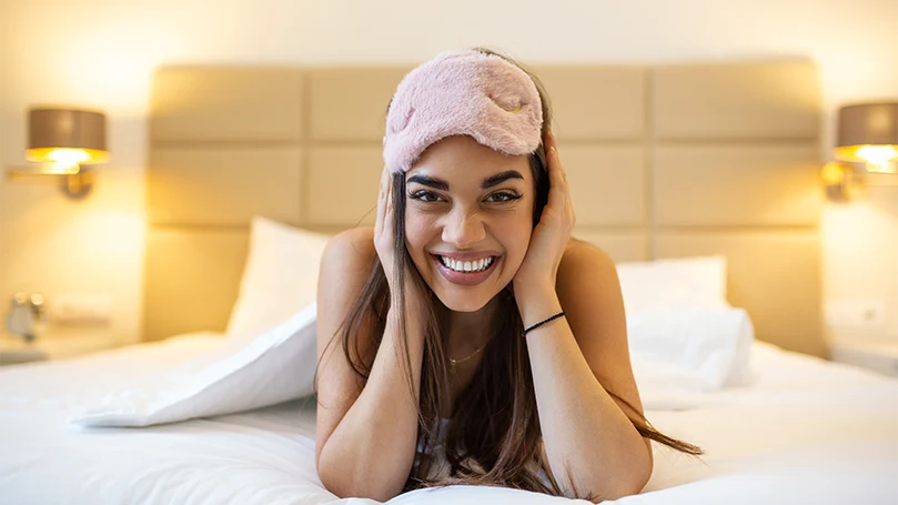 An image of a young beautiful woman on a bed with eye mask.