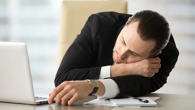An image of a business man had fallen asleep in the office due to narcolepsy condition.