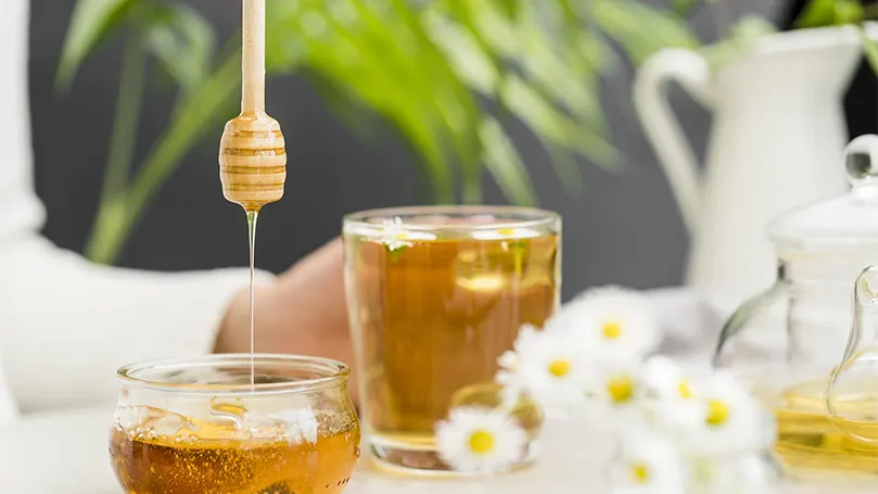 A glass of tea and honey spoon.