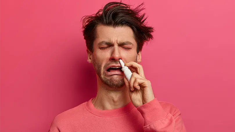 An image of a man suffering from allergies and using nasal drops.