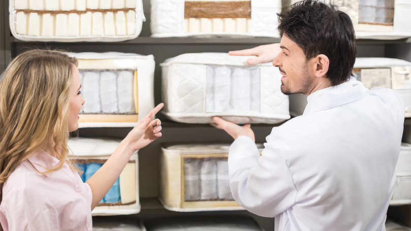 A salesman tells customer about quality mattresses in store.