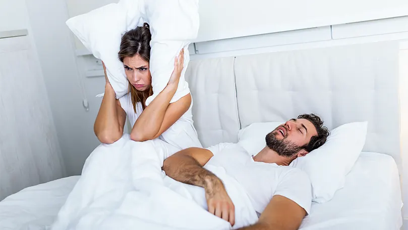An image of a woman having problems with a man who snores in bed.