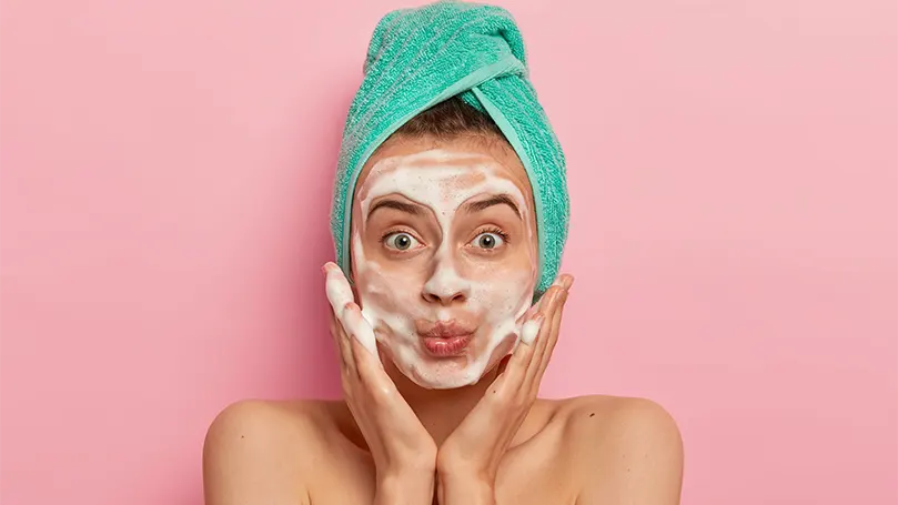 An image of a woman putting on her face a face cleanser.