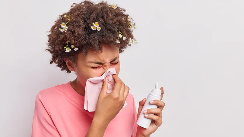 An image of a young woman blows her nose due to allergies.