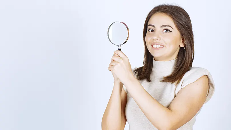 An image of a young woman holding a magnifier.