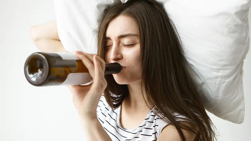 An image of a woman drinking alcohol in bed.