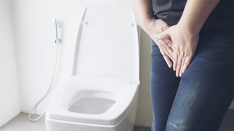 An image of a woman holding her bladder due to peeing need next to toilet.