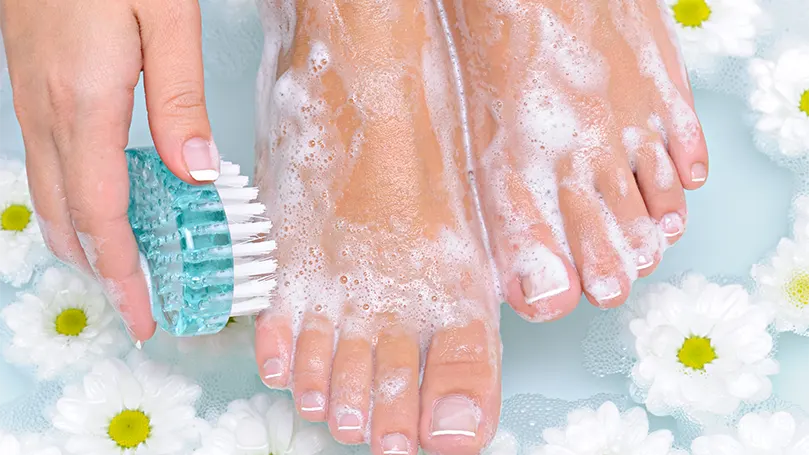 An image of a woman soaking and scrubbing her feet in warm water.