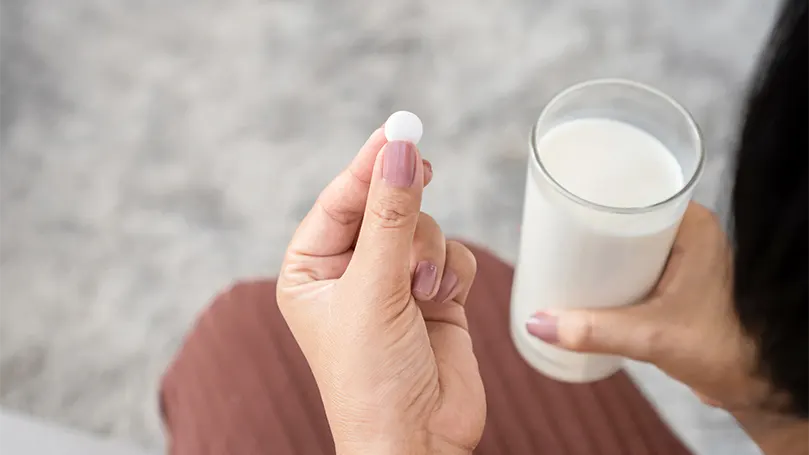 An image of a woman taking a melatonin pill with glass of milk.