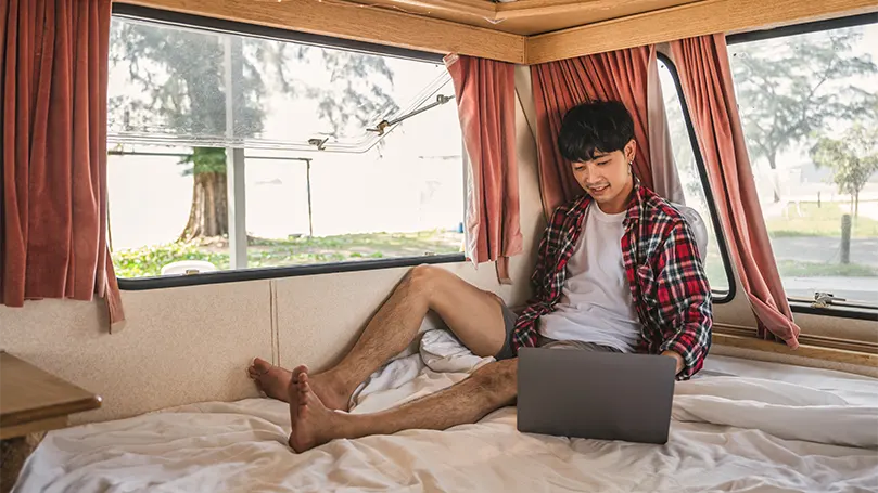 An image of an Asian man with laptop on a caravan mattress.