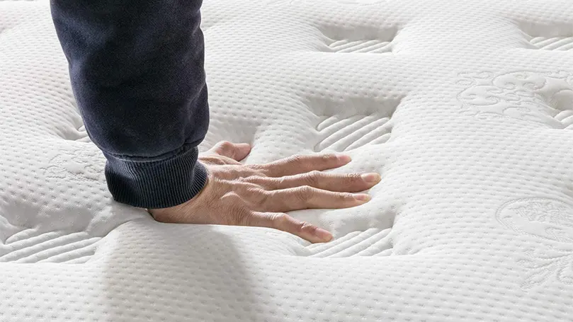 An image of a man pressing plush mattress with hand.