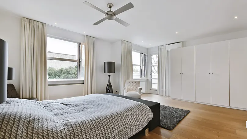 An image of a minimalistic bedroom with a fan in ceiling.