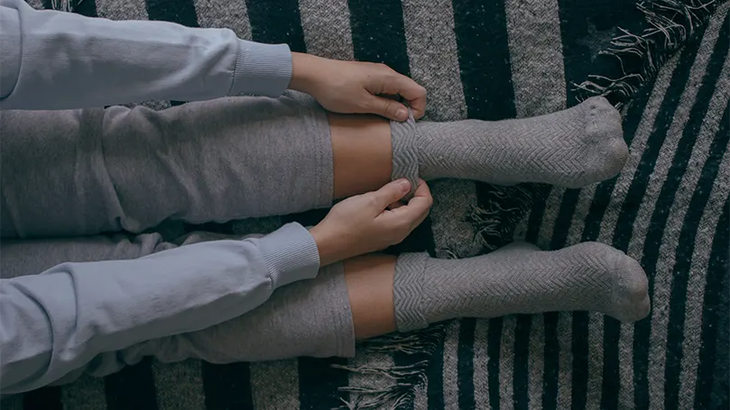 An image of a woman putting her socks on in bed.