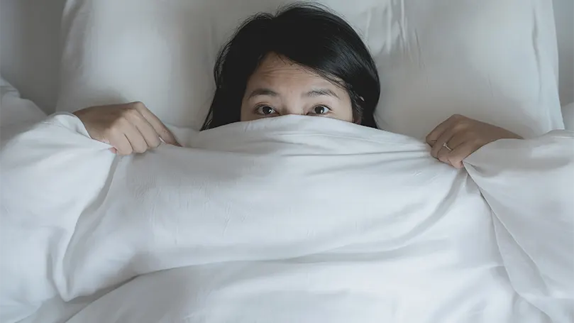 An image of a woman scared behind a blanket.