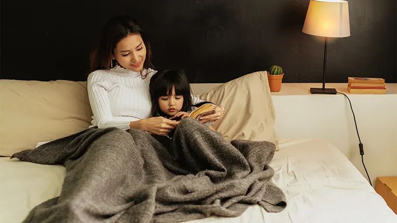 An image of a young asian mother with her daughter in bed preparing for sleep.