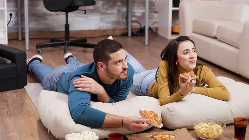 An image of a couple on the floor eating pizza.