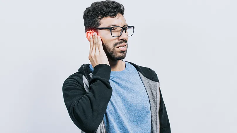 A young man with glasses suffering from ruptured eardrum.