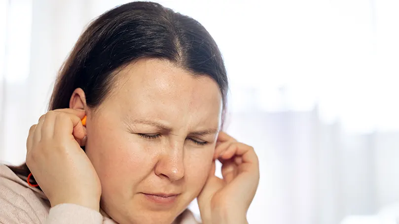 A woman holding her ears due to problems with ruptured eardrum.