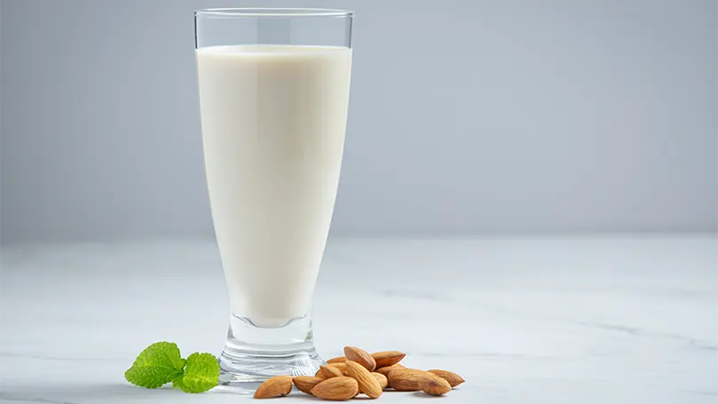An image of almond milk in a glass with almonds to the side