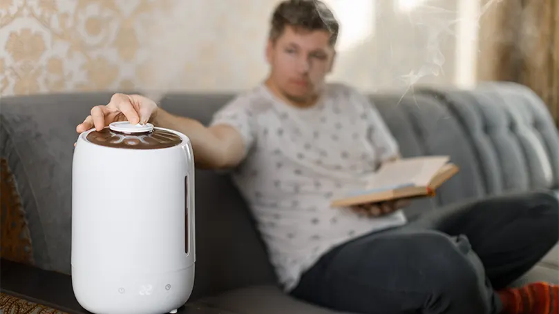 A young man reading a book on couch and setting up humidifer