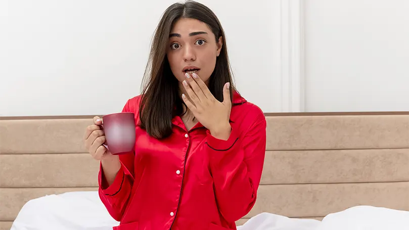 An image of a woman in red pajama drinking water due to waking up due dry mouth.