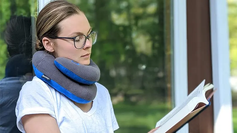 An image of a woman reading a book while using Bcozzy Chin Supporting Travel pillow.