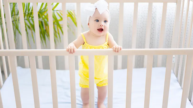 An image of a baby standing in a cot bed.