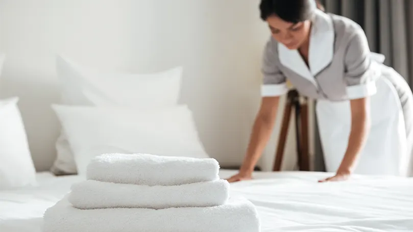 An image of a hotel maid making a bed in a hotel.