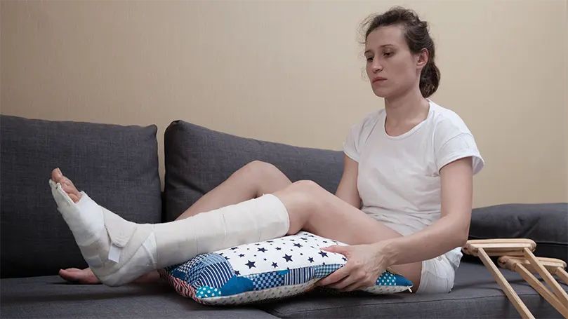 An image of a woman on couch with a pillow under her knee.