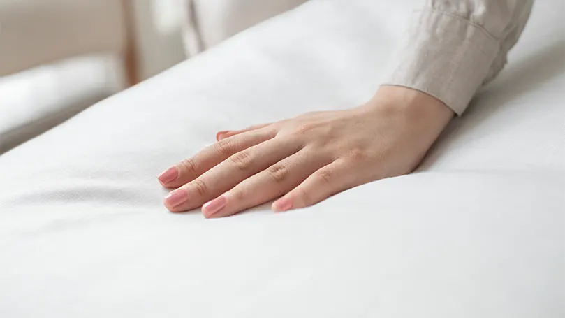 A hand pressing down on a mattress.