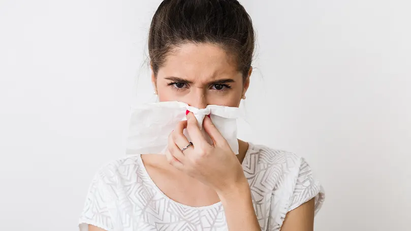 A woman blowing her nose due to allergies