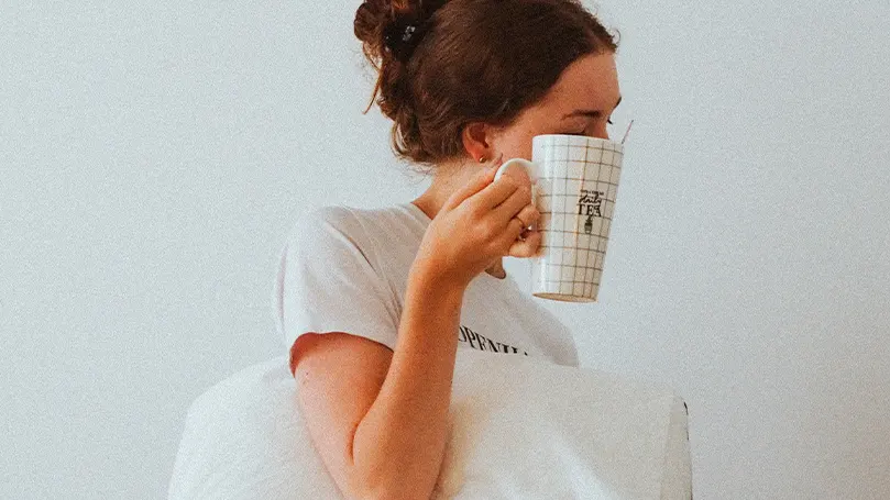 An image of a woman waking up from sleep and drinking tea as part of her morning routine