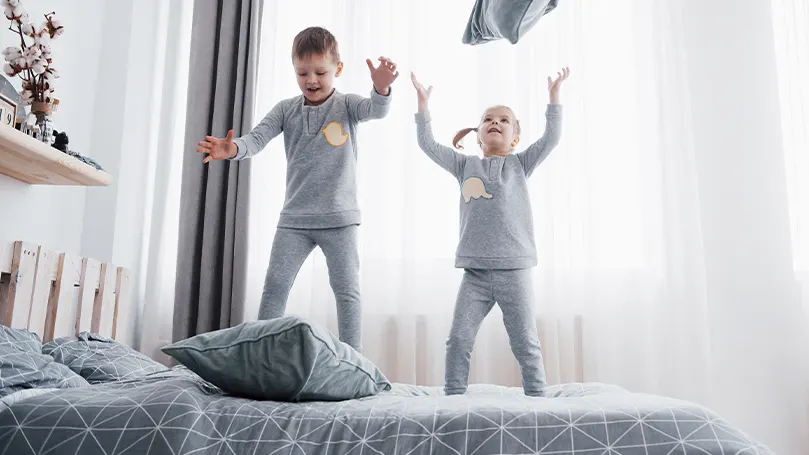 An image of two young kids jumping on the bed.
