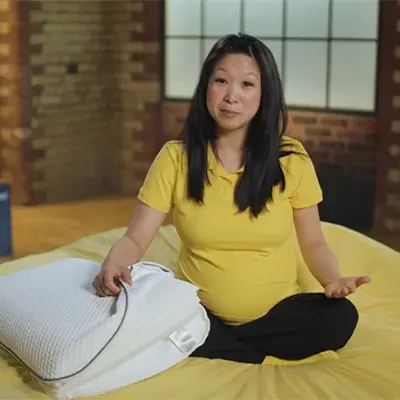 our presenter Bo holding Emma Original pillow and sitting on a bed in our studio