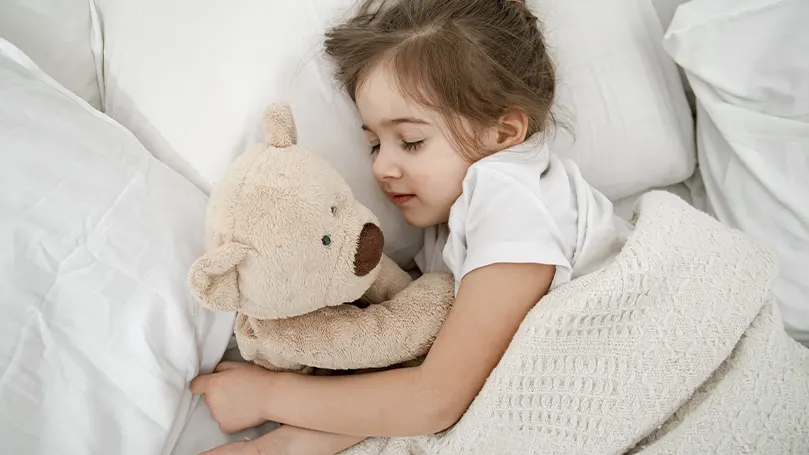 An image of a little girl being cosy in bed with her stuffed animal