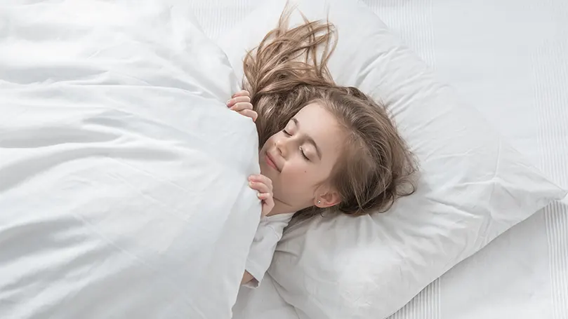 An image of a child sleeping in bed covered with a duvet