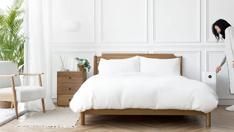 An image of a woman in a bedroom with white sheets