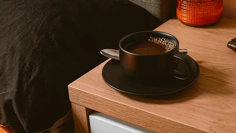 An image of a nightstand with a cup of coffee on it.