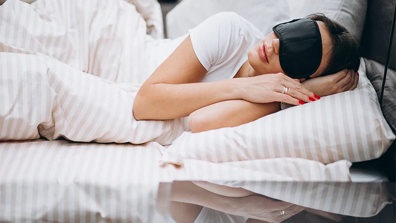 An image of a woman with a sleep mask sleeping in bed