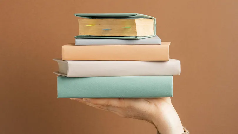 An image of a hand holding stacked books.
