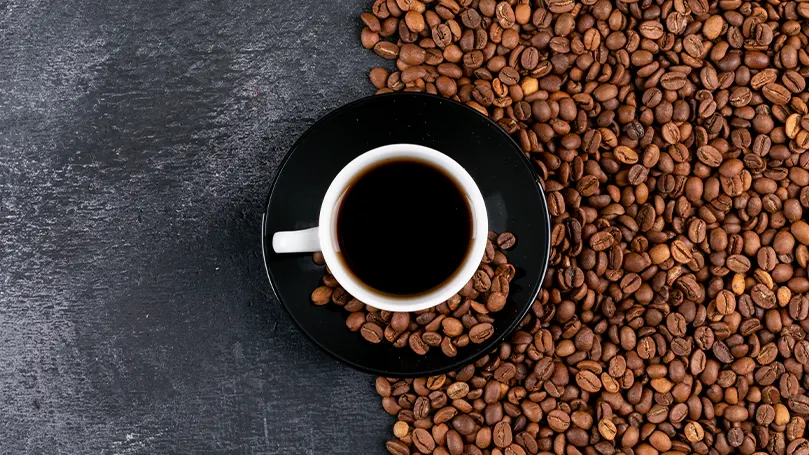 An image of a cup of coffee surrounded by coffee beans