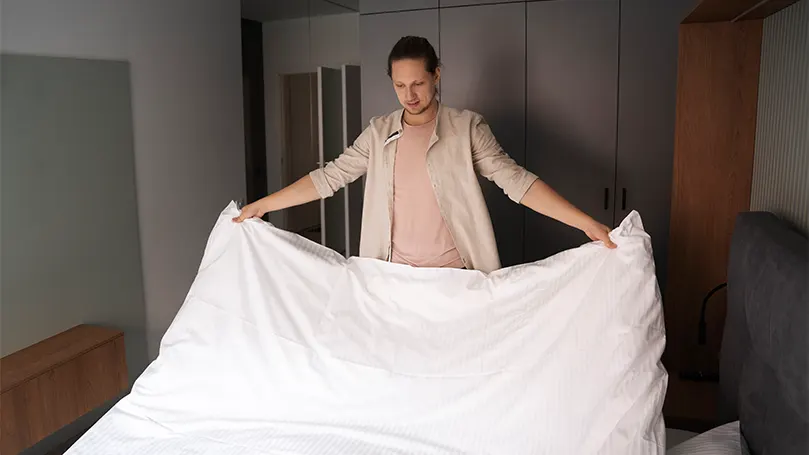 An image of a man putting on a duvet cover on a duvet.