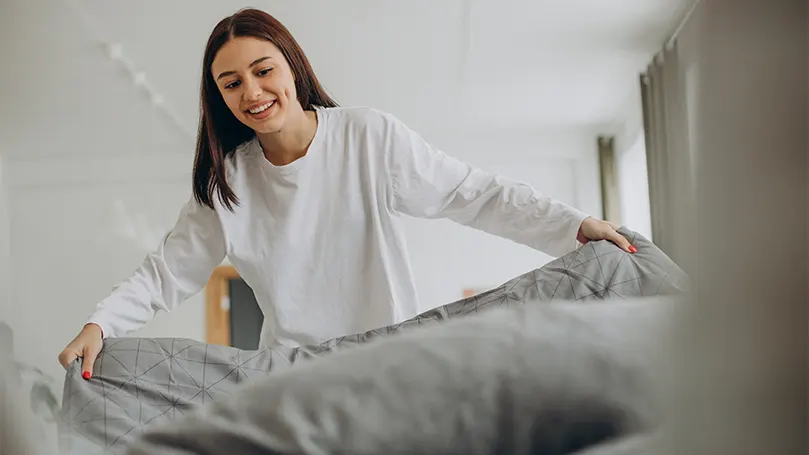 An image of a happy woman making her bed.