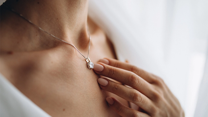 An image of a woman with a necklace touching the pendant