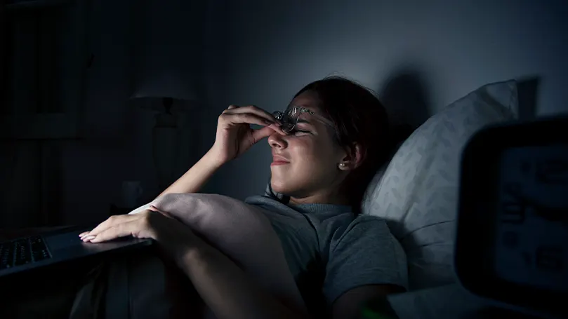 An image of a woman in bed at night holding her face in pain
