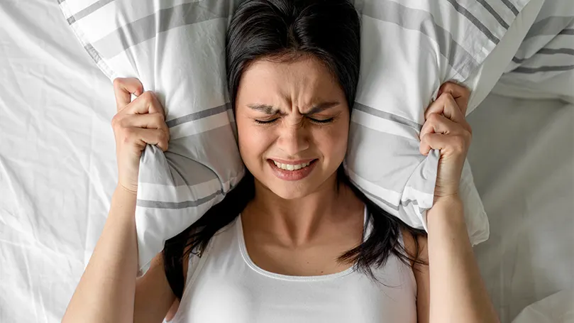 An image of a woman covering her ears with her pillow