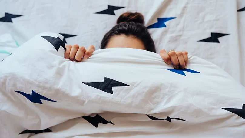 An image of a woman covering her face with a duvet.