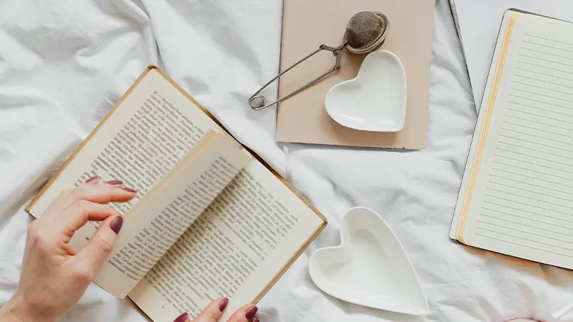 An image of a person reading a book on bed.